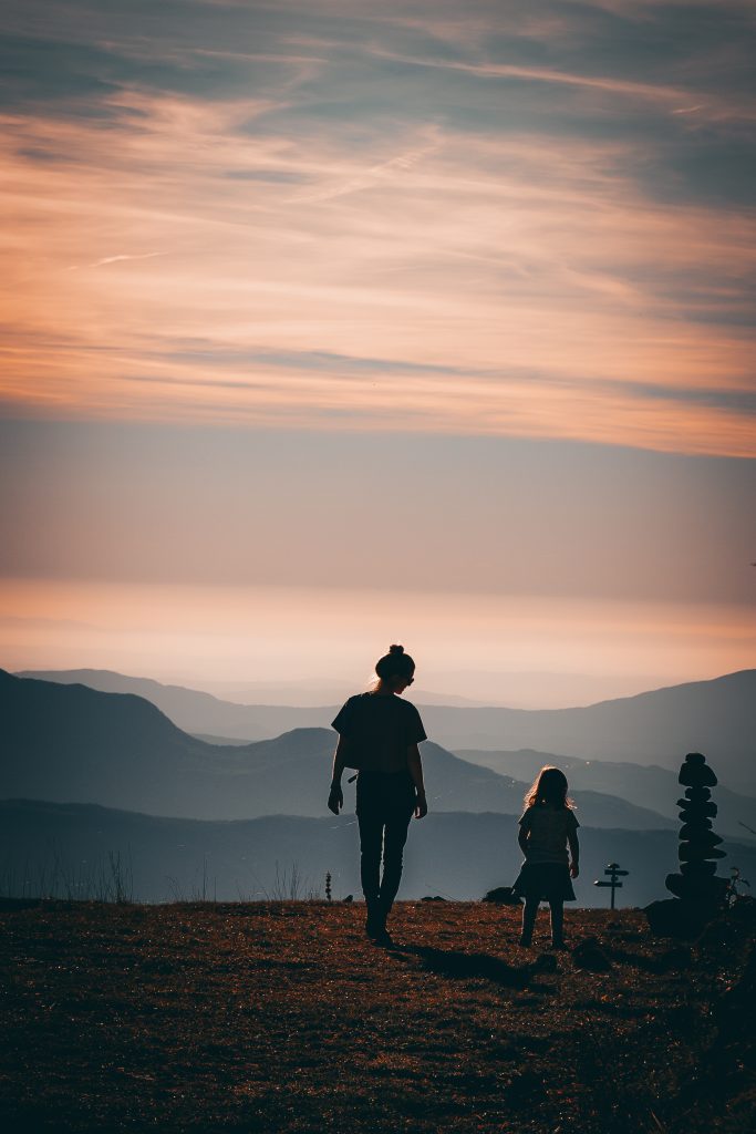 Mutter und Tochter laufen während eines dokumentarischen Familienshootings in den Alpen in Richtung des Sonnenuntergangs.