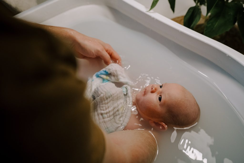 Ein Neugeborenes wird das erste Mal liebevoll von seinem Vater gebadet.